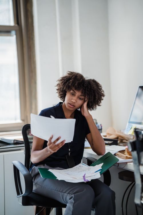 Free A professional woman with curly hair reviews documents at her office desk, deep in thought. Stock Photo