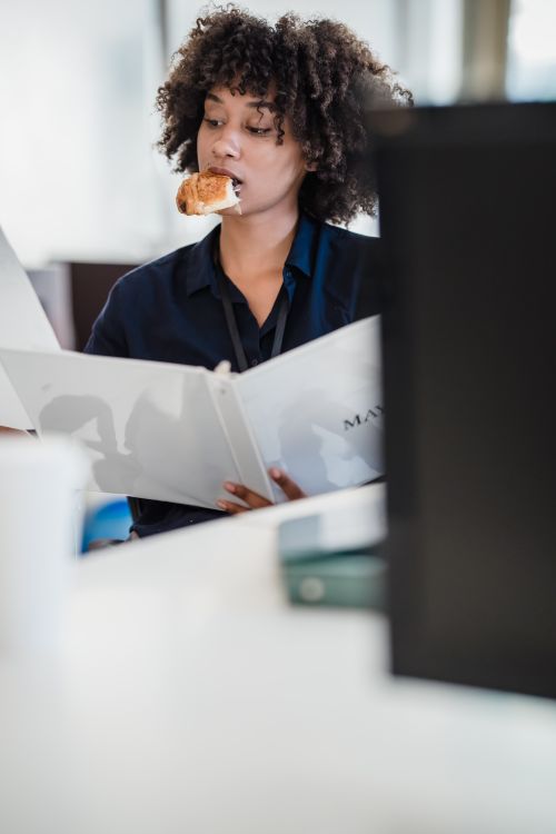 Free Office scene of a woman multitasking by reviewing documents while eating. Stock Photo