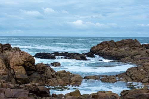 Free Serene rocky coastline under a cloudy sky, with waves gently crashing on the rocks. Stock Photo
