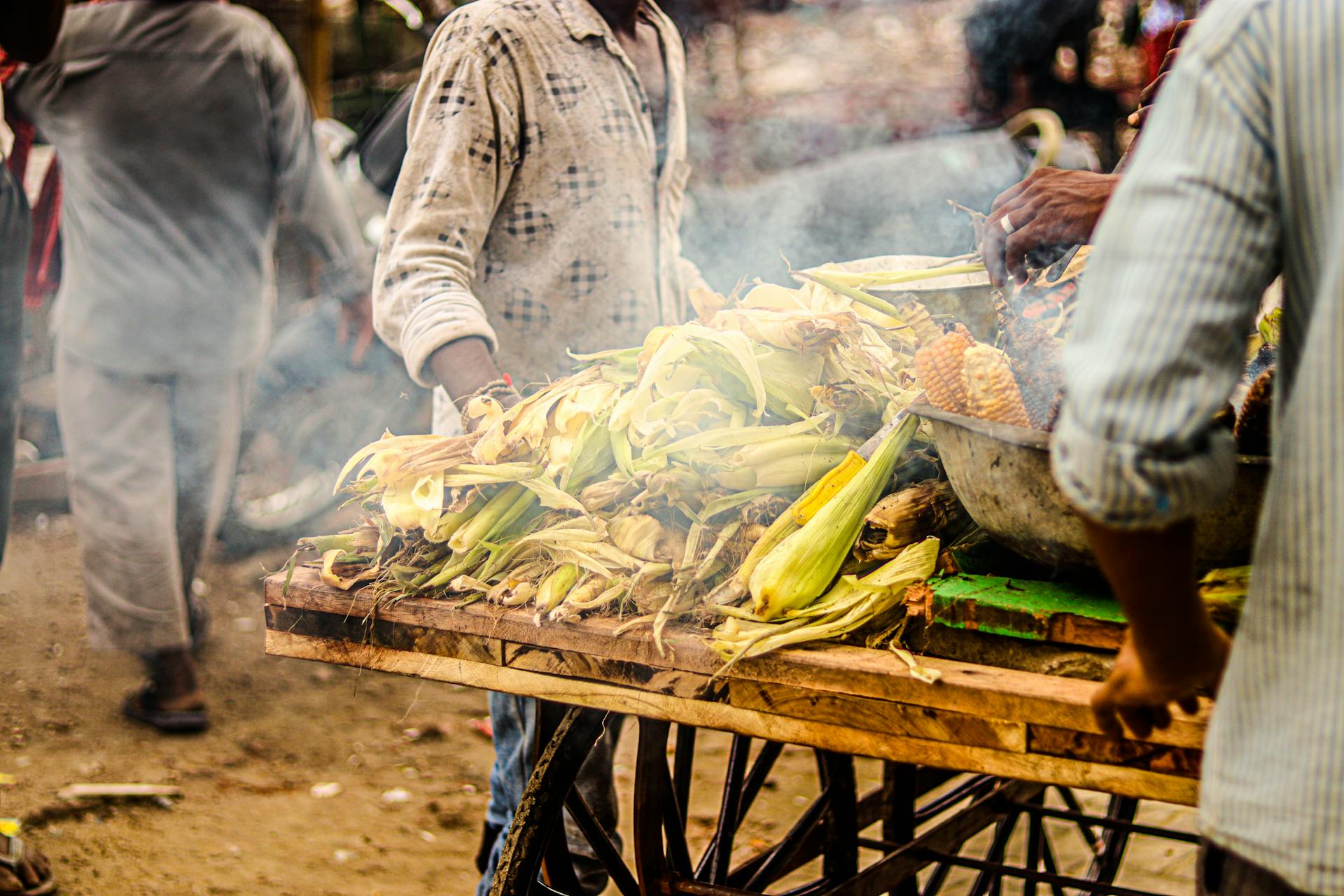 People Cooking Corncobs on Street Market