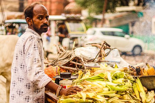 A street vendor selling fresh corn on a vibrant city street with vehicles passing by.