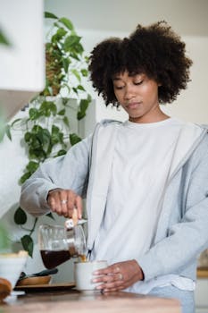 A woman pours coffee in a cozy kitchen setting, surrounded by greenery, embodying a relaxed morning vibe.