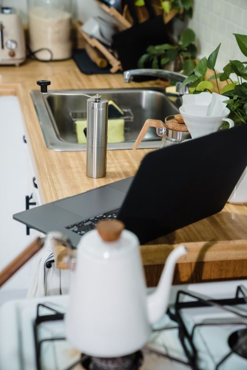 Free A modern kitchen counter with a laptop, coffee maker, and plants, showcasing a cozy home workspace. Stock Photo