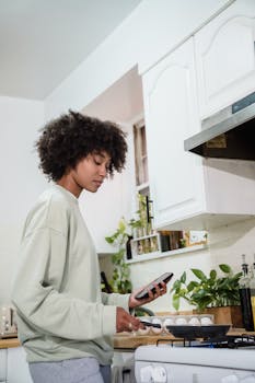 African American woman cooking in a kitchen while checking her smartphone