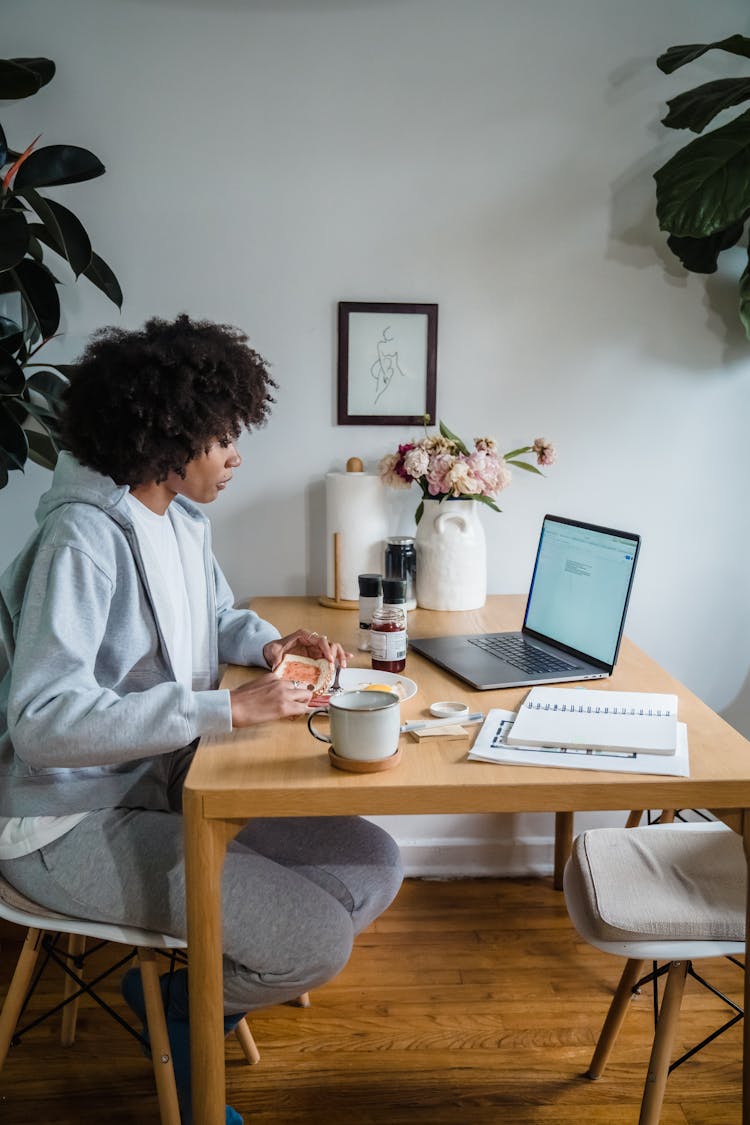 Woman Eating At Home Table With Laptop