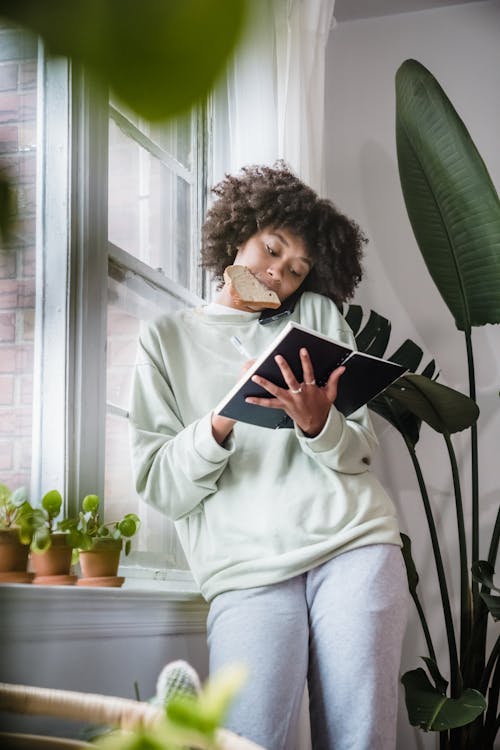 Woman Eating Toast Writing in Notebook