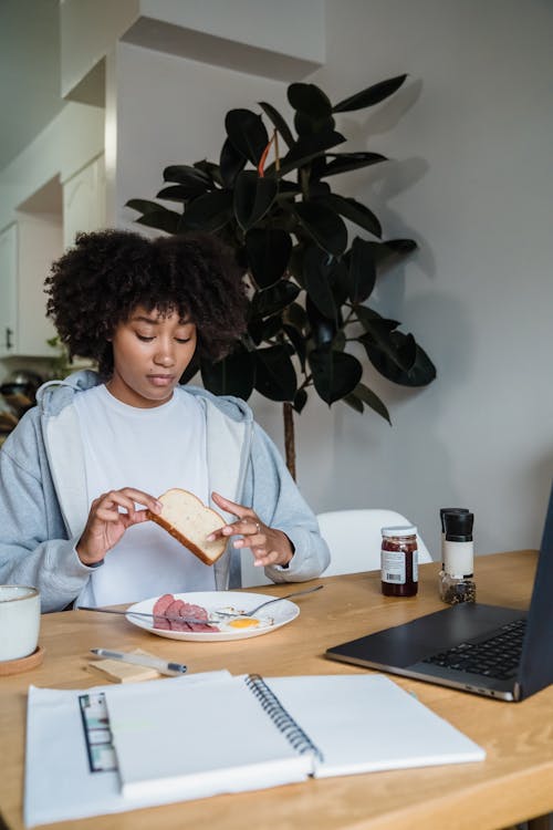 Free Woman Eating Breakfast Using Laptop at Home Stock Photo