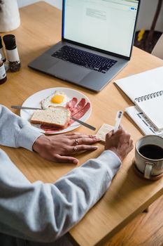 A woman multitasks with breakfast and work at home, featuring eggs, toast, and coffee.