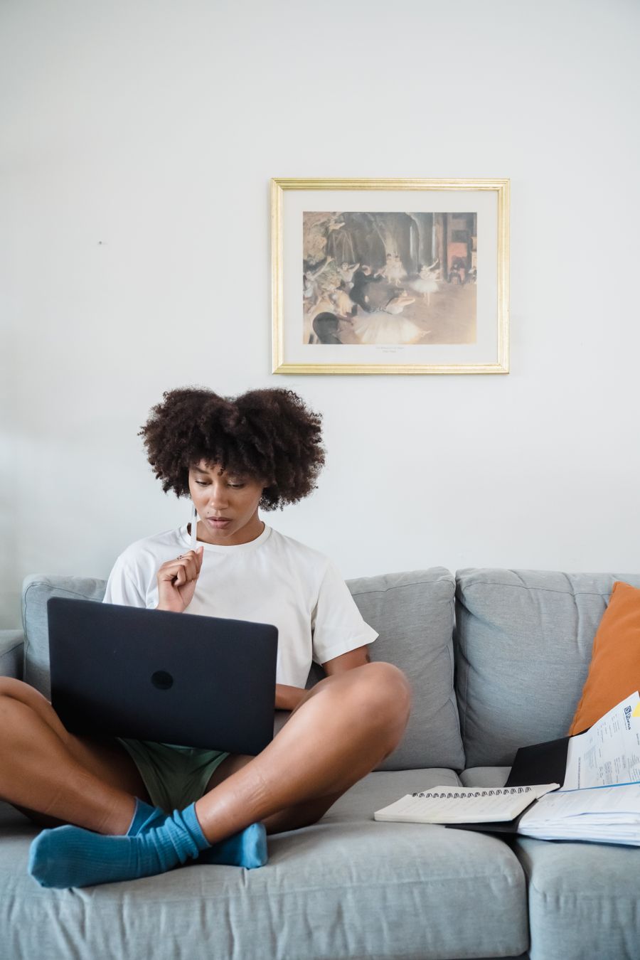 A woman sits on a grey sofa working on a laptop