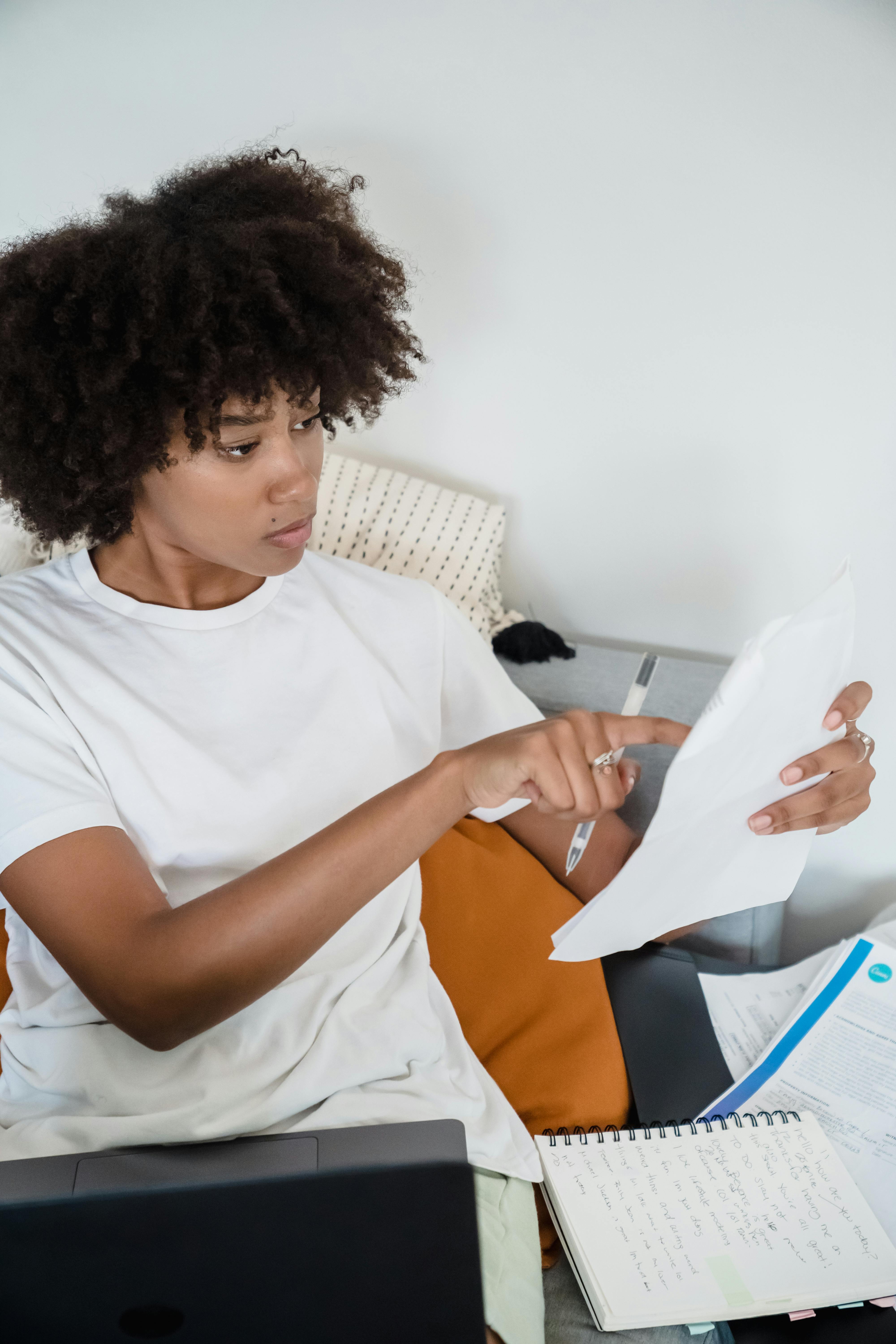 Free Young woman reviewing documents and working on a laptop from home. Remote work lifestyle. Stock Photo