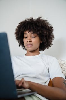 Young woman with curly hair working remotely on a laptop, focused on screen