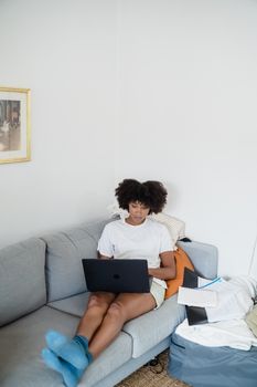 Young woman working on a laptop in a cozy living room, illustrating remote work lifestyle.