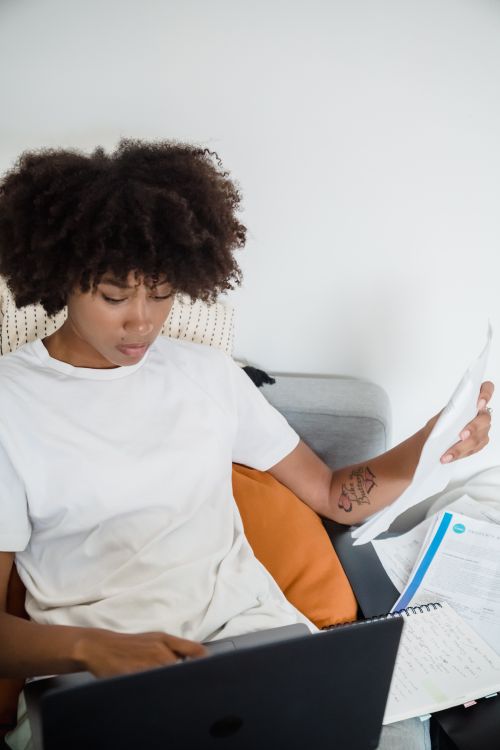 Free Young woman working remotely on laptop with documents at home, demonstrating focused work environment. Stock Photo