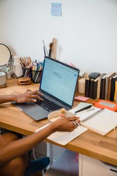 Woman multitasking with laptop and noodles at a home office desk, showcasing productivity and remote work.