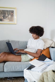 African American woman sitting on couch working remotely on laptop.