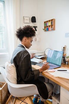 African American woman working on a laptop at home office desk, focused on tasks.