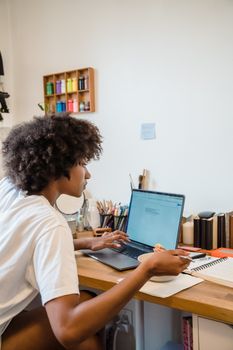 A young woman engaged in remote work on her laptop at a home desk setting.