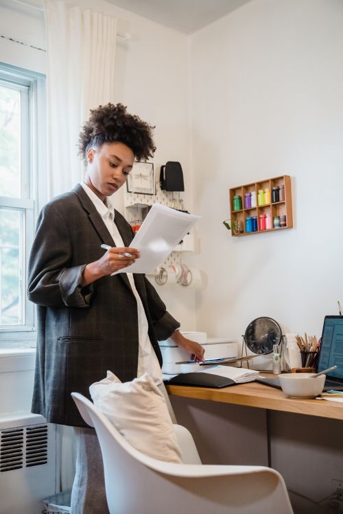 Free Young woman in home office reviewing documents by the desk with tech setup. Stock Photo