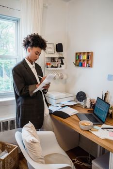 Businesswoman in a home office setting reviewing documents beside a laptop and printer.