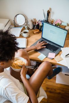 Woman multitasking, eating lunch while using a laptop at a workstation.