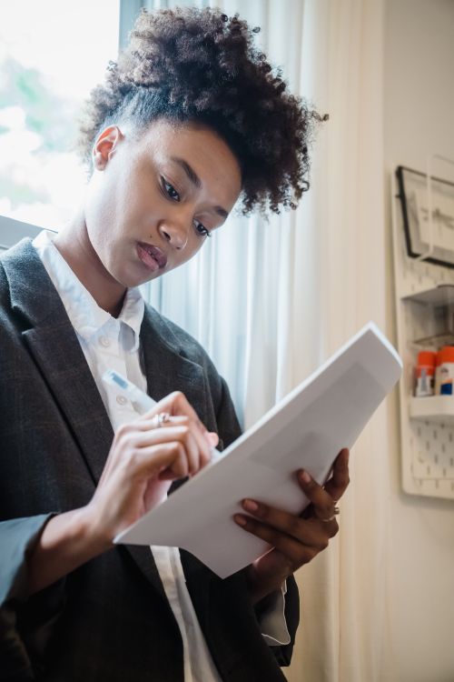 Free Young woman in suit writing on paper inside a well-lit room. Stock Photo