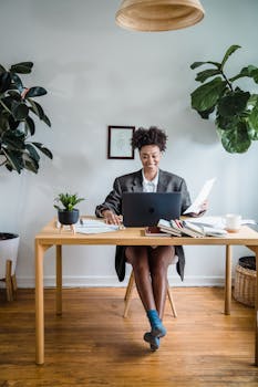 Smiling woman engaged in video call while working at her home office desk surrounded by plants