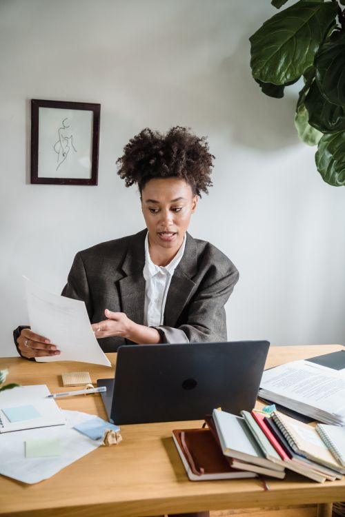 Free Confident woman engaged in work discussion, holding documents at her desk with a laptop. Stock Photo