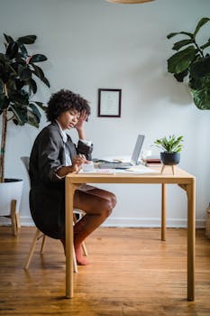 Woman with curly hair working on a laptop in a modern home office with plants.