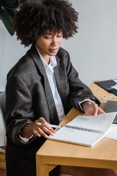 Free Businesswoman organizing and planning with a notebook at her office desk wearing casual blazer. Stock Photo