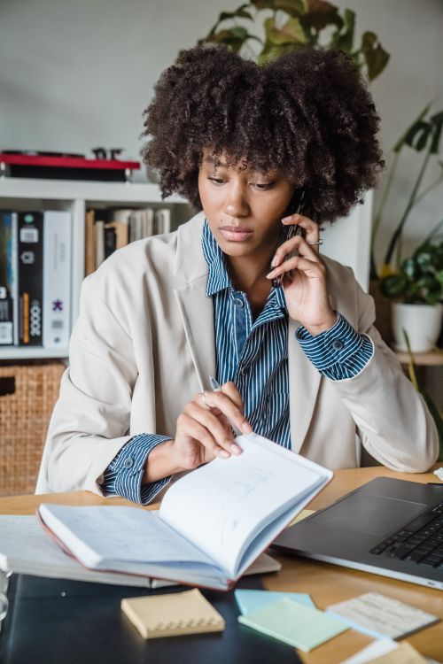 Free Focused woman multitasking in modern office with phone and notebook. Stock Photo