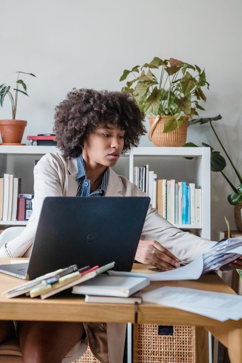 Free Focused businesswoman working at desk with laptop, organizing paperwork in a modern home office setting. Stock Photo