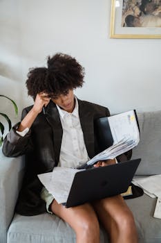 Woman multitasking at home juggling laptop and documents.