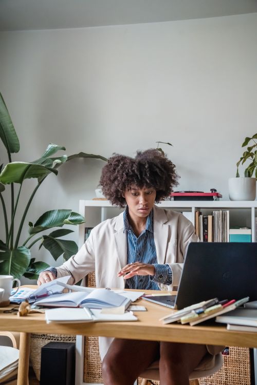 Free Focused woman working from home with laptop and books, surrounded by plants. Stock Photo