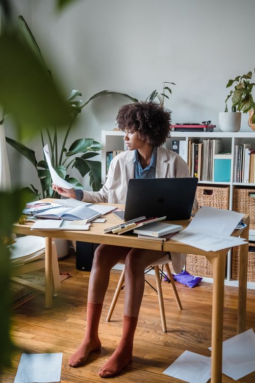 Free Woman with curly hair working on a laptop in a modern home office setting. Stock Photo