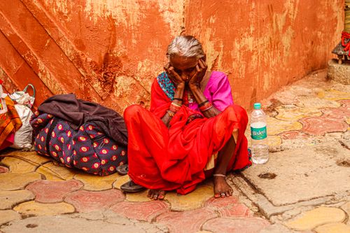 Free An elderly woman rests against a wall, wearing vibrant traditional attire, conveying a sense of solitude. Stock Photo