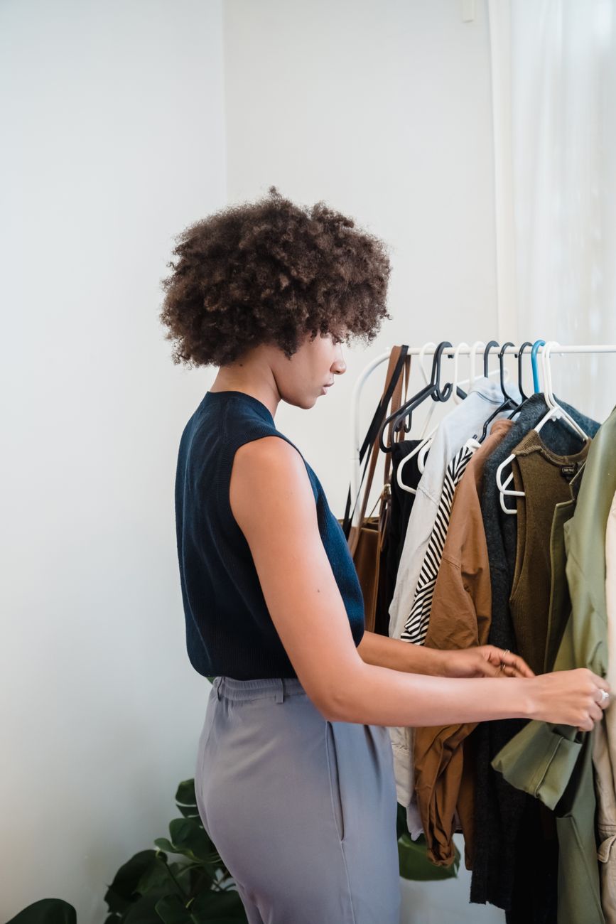 Woman with curly hair selecting clothes from indoor rack. Fashion and style concept.