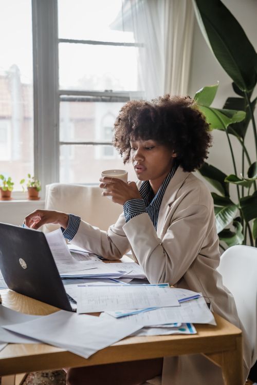 Free Woman drinking coffee, surrounded by documents, working remotely from home. Stock Photo