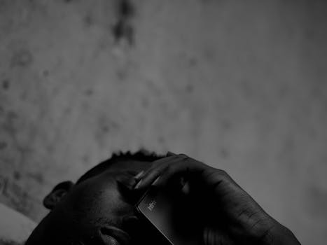 A black-and-white close-up of a man using a smartphone outdoors in Rujewa, Tanzania.