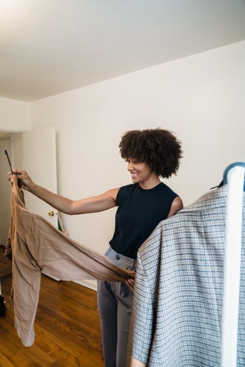 Free Smiling woman selecting outfit from clothing rack in a stylish room. Stock Photo