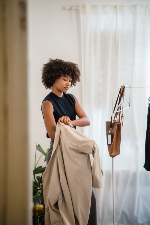 Free A fashionable woman tries on a coat in a chic room with natural light and decor. Stock Photo
