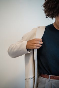 A stylish woman adjusting a beige blazer over a navy top, showcasing modern fashion.