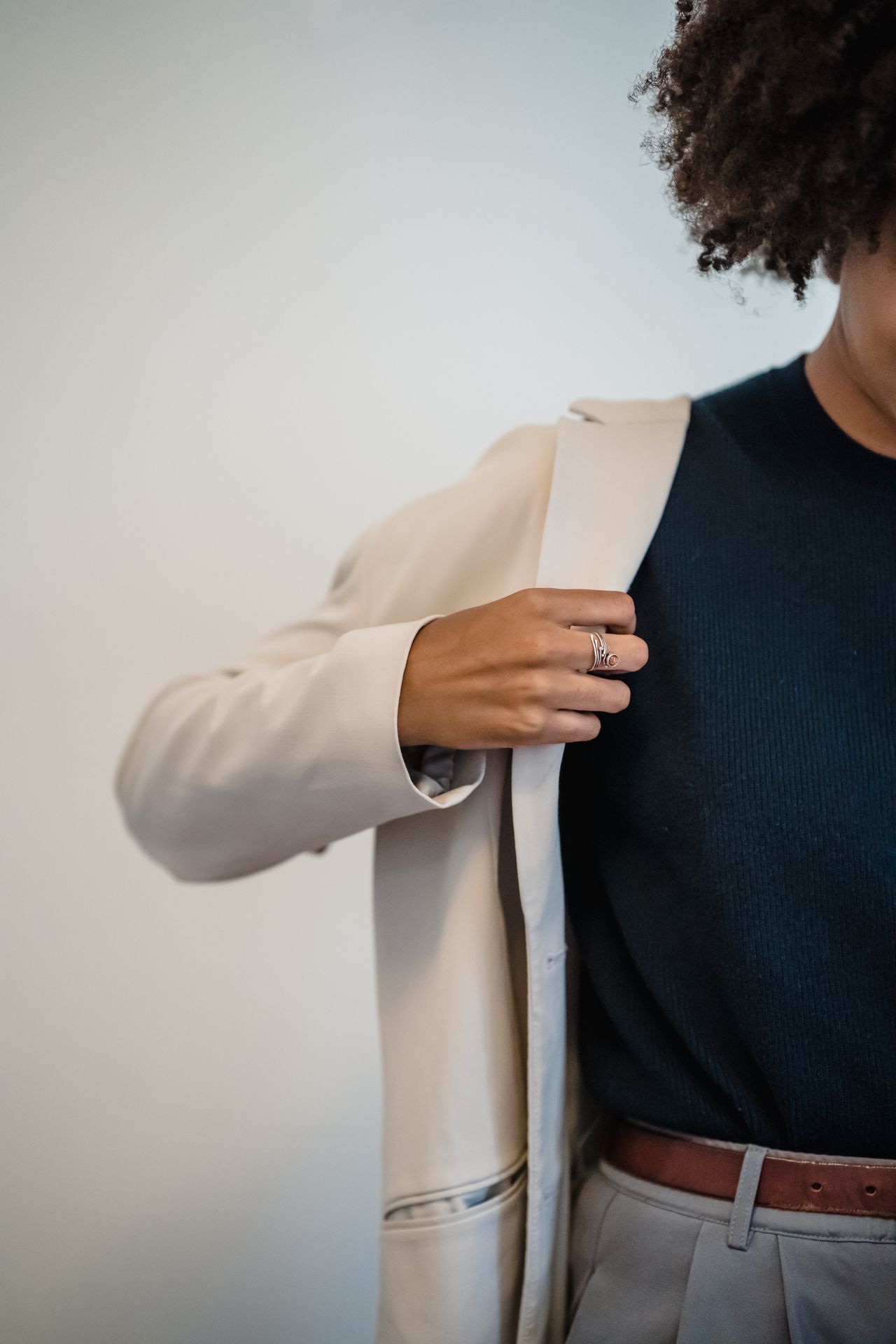 Cream blazer worn open over a dark top with a brown leather belt marking the waist