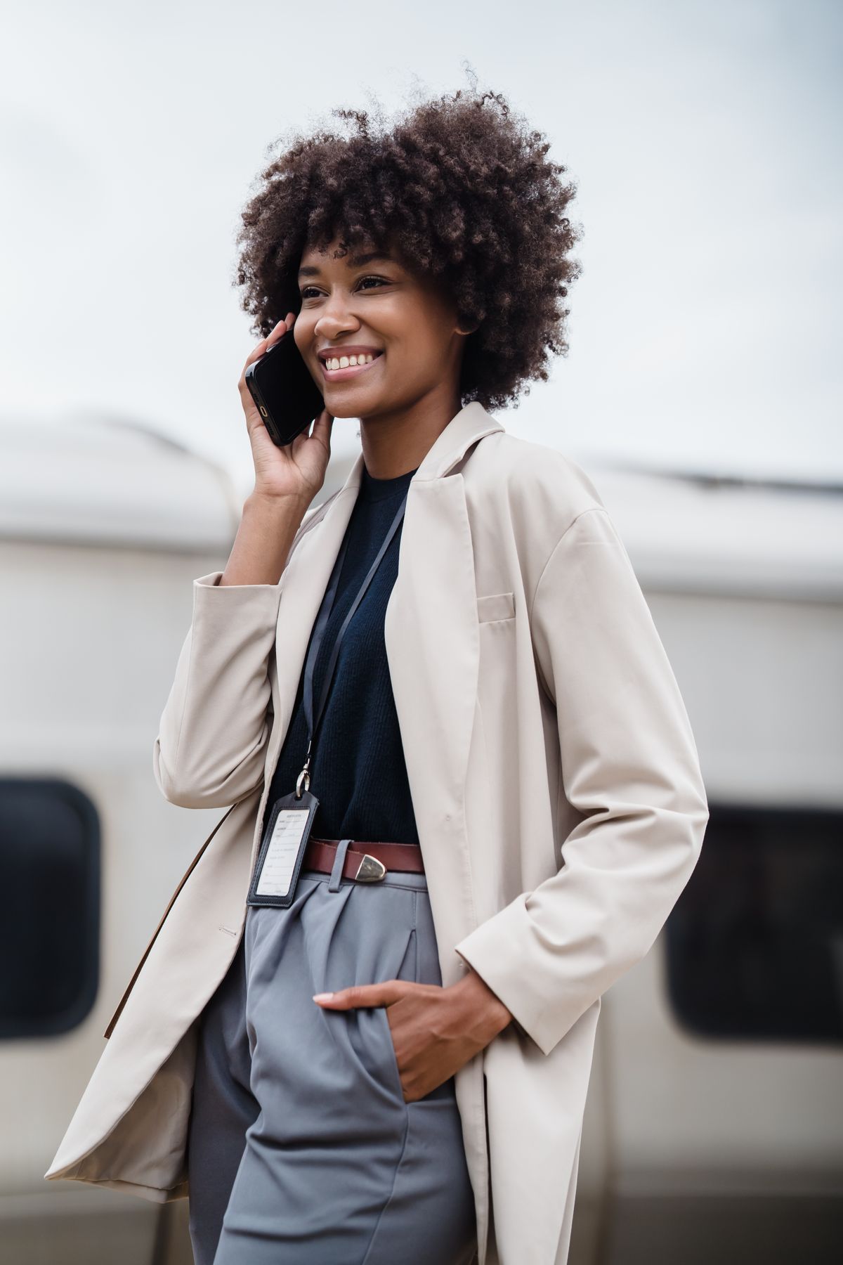 A smiling woman talking on her phone, reassured, with a vehicle blurred in the background