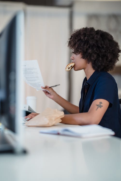 Woman Eating Pastry while Sorting Docum