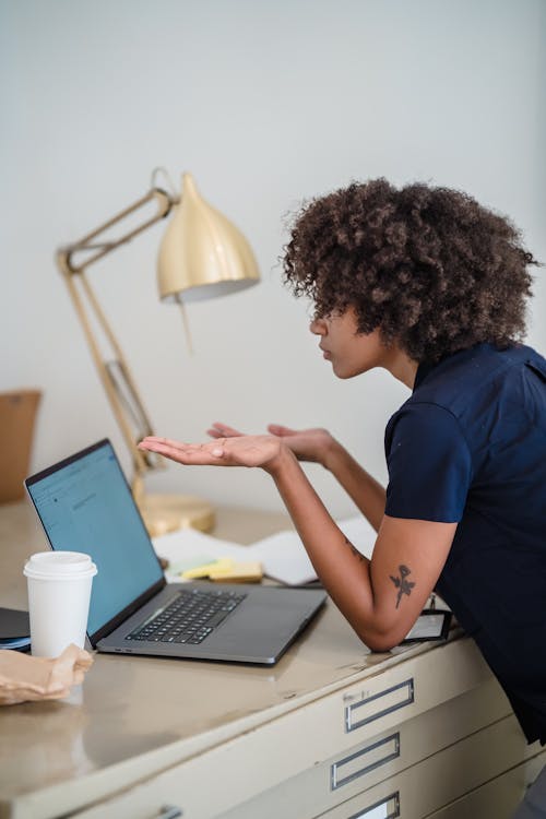 Woman Sitting Behind a Desk, Using Laptop and Spreading Her Hands as a Sign of Not Understanding Something 
