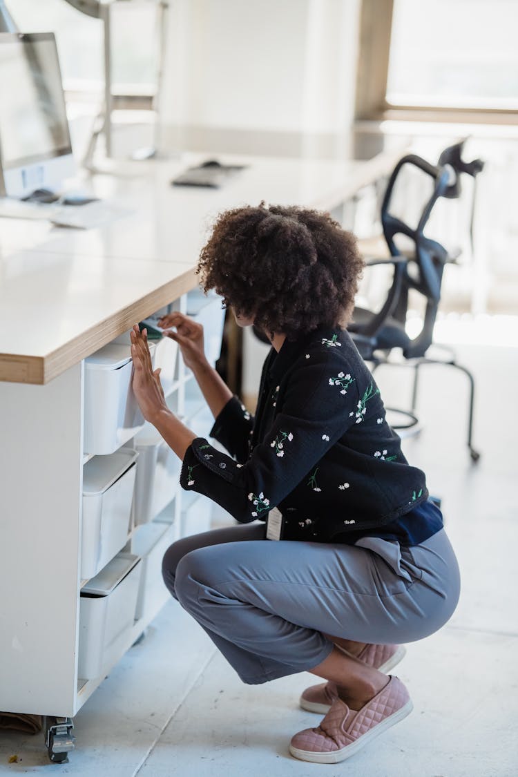 Woman Crouching And Looking For Something In A Box In An Office Desk 