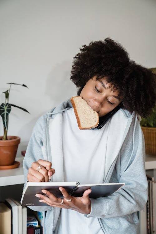 Woman in Casual Clothing Taking Notes and Eating 