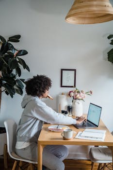 Woman working remotely with breakfast in a cozy home office setting.