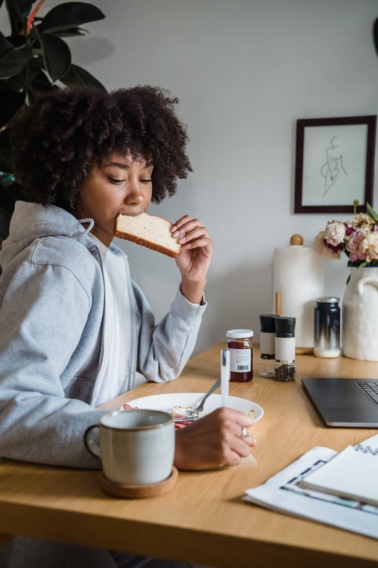 Woman Eating At Her Desk With Pen In A Hand