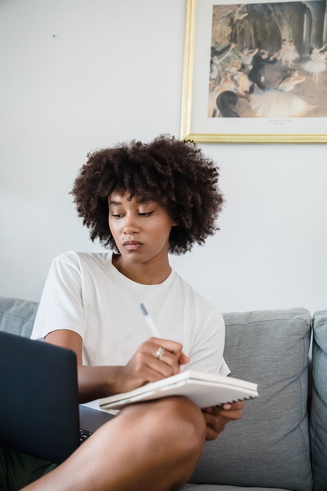 A woman studying on a sofa with a notebook open on her knee